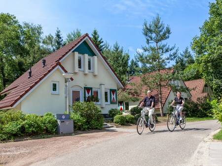 Man en vrouw fietsen voor enkele vakantiehuizen op vakantiepark Landal De Vers