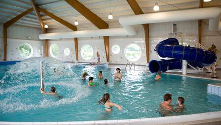 Mensen aan het zwemmen in het binnenbad met glijbaan op vakantiepark Molecaten Park Flevostrand