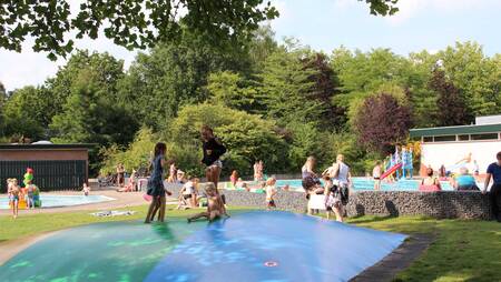 Kinderen springen op de aitrampoline bij het zwembad van Molecaten Park Landgoed Ginkelduin