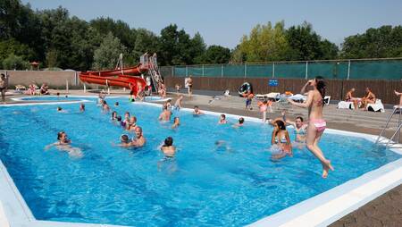 Mensen zwemmen in het buitenbad met grote rode glijbaan op vakantiepark Molecaten Park Rondeweibos