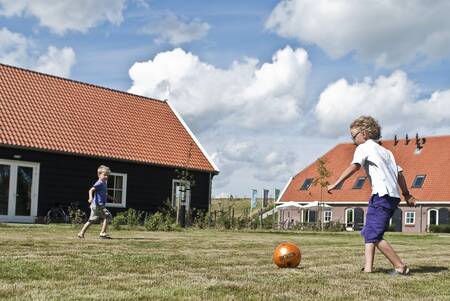 Kinderen aan het voetballen tussen vakantiehuizen op Oosterscheldepark De Stelhoeve