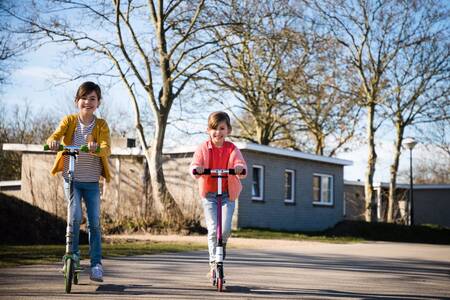 Twee kinderen steppen voor chalets op vakantiepark RCN Toppershoedje