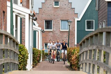 Gezin fietst tussen de vakantiehuizen naar een brug op vakantiepark Roompot Marinapark Volendam